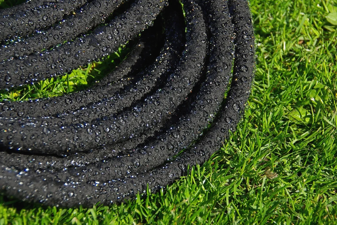 Schwarzer Gartenschlauch auf Rasen